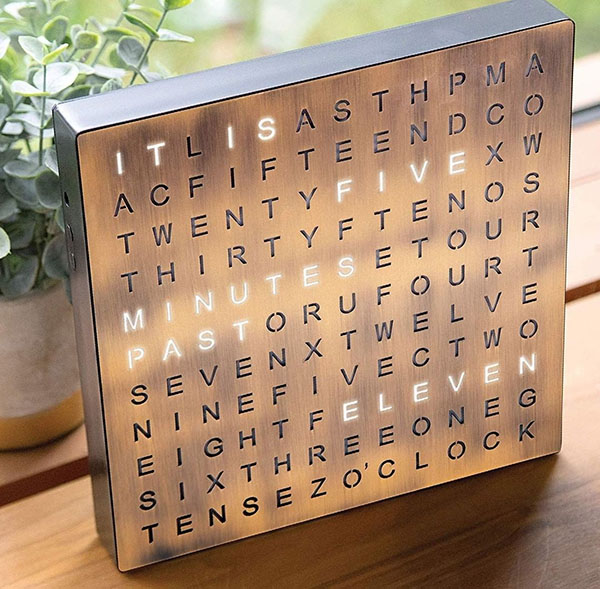 A word clock sitting on a wooden shelf. It reads: 'It is five minutes past eleven'
